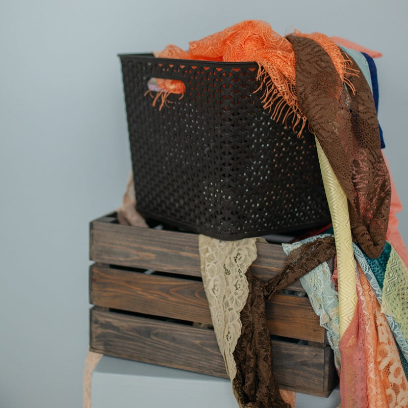 A black casket filled with textiles in varying colors stacked on top of a wooden box