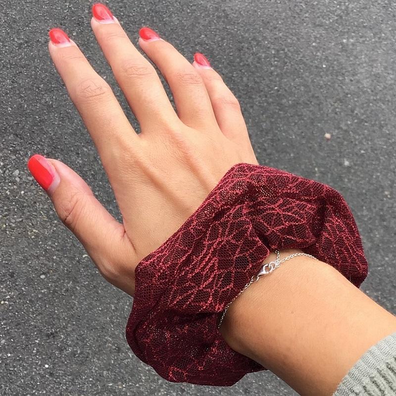 Hand with orange painted nails showing off a dark red scrunchy on the wrist