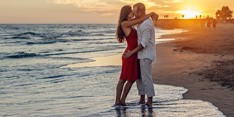 2 people kissing on a beach at sunset